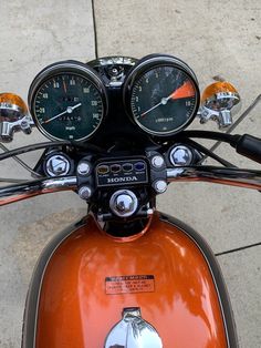 the handlebars and gauges are visible on an orange scooter