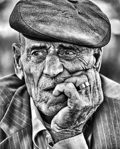 an old man wearing a hat and holding his hand to his face while looking at the camera