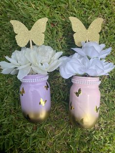 two vases with flowers and butterflies on them sitting in the grass next to each other