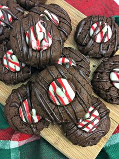 chocolate cookies with white and red candy canes are on a wooden board next to a plaid cloth