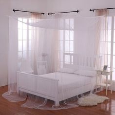 a white bed sitting on top of a hard wood floor next to two windows with sheer curtains