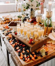 a wooden table topped with lots of glasses filled with champagne and fruit on top of it