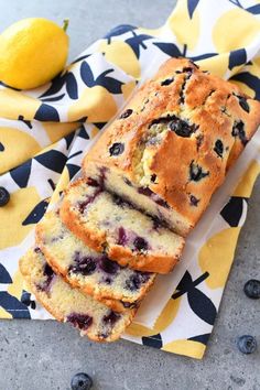 a loaf of blueberry bread sitting on top of a yellow and black towel next to two lemons