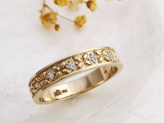 a yellow gold ring with small diamonds on it next to some dried flowers and leaves