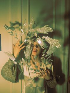 a woman in a white dress is holding her hands up to her face while wearing a silver bird headdress