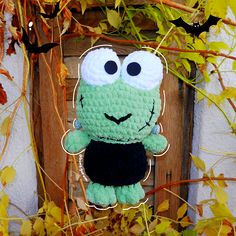 a crocheted green stuffed animal hanging from a wooden frame with leaves around it