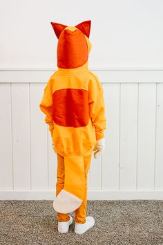 a little boy in a cat costume standing on the floor with his back turned to the camera