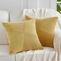 two yellow pillows sitting on top of a white couch next to a potted plant