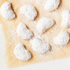 powdered sugar cookies are arranged on a piece of parchment paper, ready to be baked