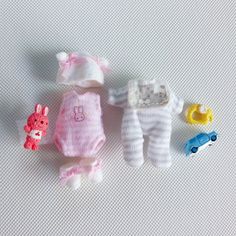 three baby dolls are laying next to each other on a white surface, one is wearing a pink onesie and the other has a toy car