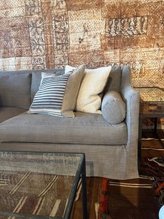 a couch with pillows on it in front of a wallpapered wall and coffee table