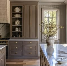 a kitchen with gray cabinets and marble counter tops, along with a vase filled with flowers