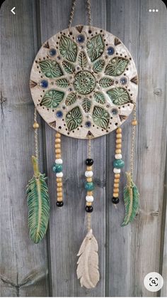 a green and white dream catcher hanging on a wooden fence with beads, feathers and beads