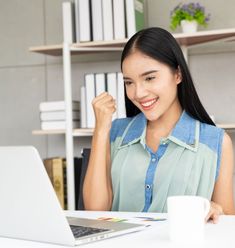 a woman sitting at a desk with a laptop computer in front of her and smiling