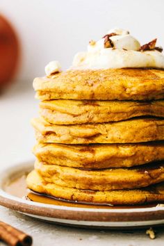 a stack of pancakes topped with whipped cream and cinnamon sticks on a plate next to an apple