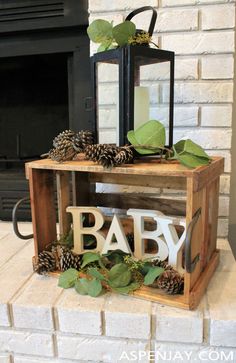 a baby sign sitting on top of a wooden crate next to a fire place filled with pine cones and greenery