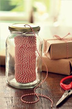 red and white twine in a glass jar next to some wrapping paper, scissors and gift boxes