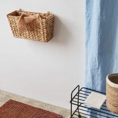 there is a basket hanging on the wall next to a rug and a potted plant