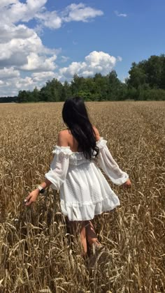 a woman in a white dress walking through a wheat field