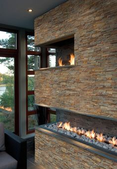 a living room with a fire place next to a large glass window that looks out onto the water