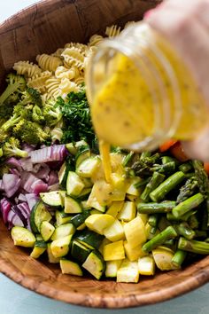 someone pouring dressing into a wooden bowl filled with vegetables