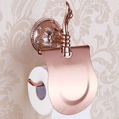 a toilet paper dispenser with a rose gold finish on the wall next to a roll of toilet paper