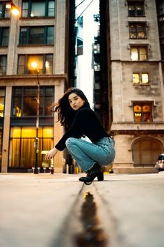 a woman kneeling down on the ground in front of tall buildings