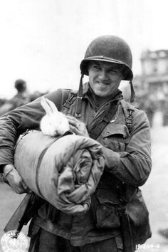 a man holding a bunny in his arms while wearing an army uniform and smiling at the camera