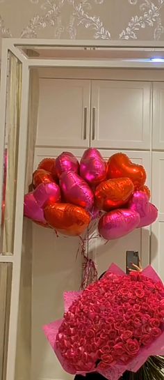 a bouquet of pink and orange balloons in front of a white wall with an open door