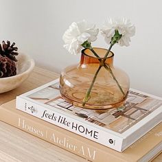 two books on a table with flowers in a vase and pine cones sitting next to them