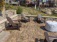 several lawn chairs sitting on top of a stone patio next to a fire pit in front of houses