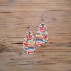 two pairs of earrings with flowers on them sitting on top of a wooden table next to a pair of scissors