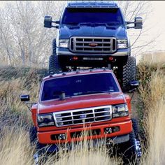 two trucks are parked on the side of a hill in front of some dry grass