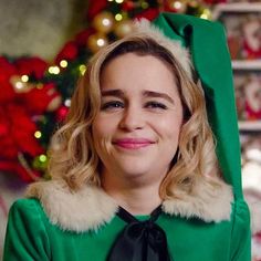 a woman in a green dress with a santa hat on her head and christmas decorations behind her