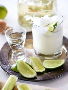 two glasses filled with ice and limes on a plate next to some sliced limes