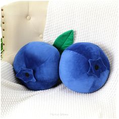 two blue fruit shaped pillows sitting on top of a white chair next to each other