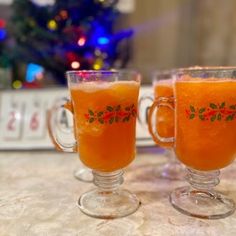 two glasses filled with orange liquid sitting on top of a table next to a christmas tree