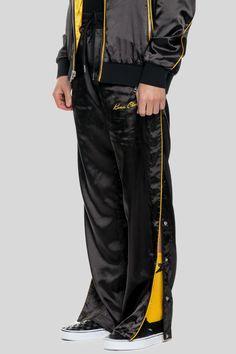 The Keiser Clark Breakaway Track Pant features a dual-sided double-faced California yellow satin body with black satin piping, twin side silver-tone zipper pockets, and an elasticated waistband. The Track Pant key features a black embroidered ‘Keiser Clark’ logo on front left leg, fully reversible body, complete breakaway snap off buttons along the outer leg for extreme functionality. Escape into the night with the jet black side or feel electric with the California Yellow side – choice is yours Black Track Jacket With Contrast Panels For Streetwear, Streetwear Track Pants, Sports Black Pants With Reflective Details, Sporty Black Pants With Reflective Details, Rudis Wrestling Pants, Yellow Track Pants, Denim Outfit Men, Yellow Satin, Black Side