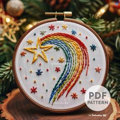 a cross stitch rainbow with stars on it in front of a christmas tree ornament