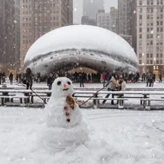 a snowman is in the middle of a city square with people walking around it