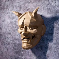 a paper sculpture of a demon head on a stone wall with the shadow of it's face