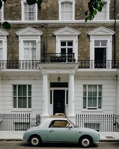 an old car is parked in front of a large white building with black wrought iron railings