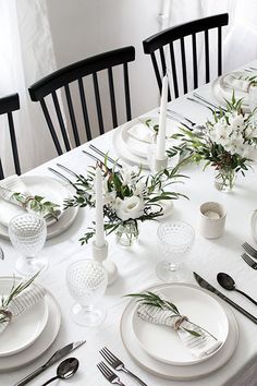 the table is set with white plates, silverware and flowers in centerpieces