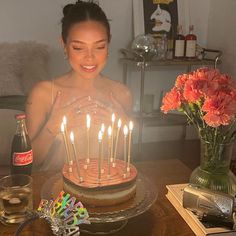 a woman sitting in front of a cake with lit candles on top of it, surrounded by flowers