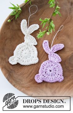 two crocheted easter bunnies sitting on top of a wooden plate