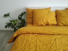 a bed with yellow sheets and pillows in a room next to a potted plant