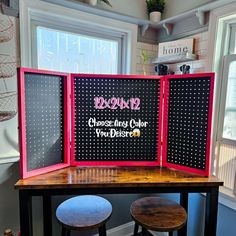 two black and pink signs sitting on top of a wooden table next to stools