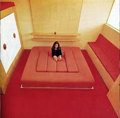 a woman sitting on top of a bed in a room with red carpet and white walls