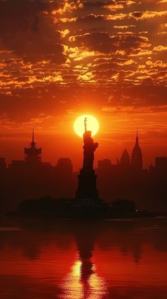 the sun is setting behind the statue of liberty