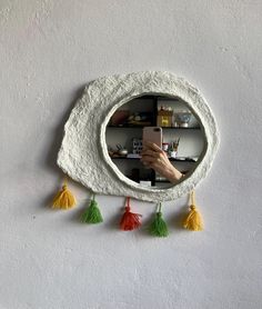 a hand holding a cell phone in front of a circular mirror with tassels hanging from it